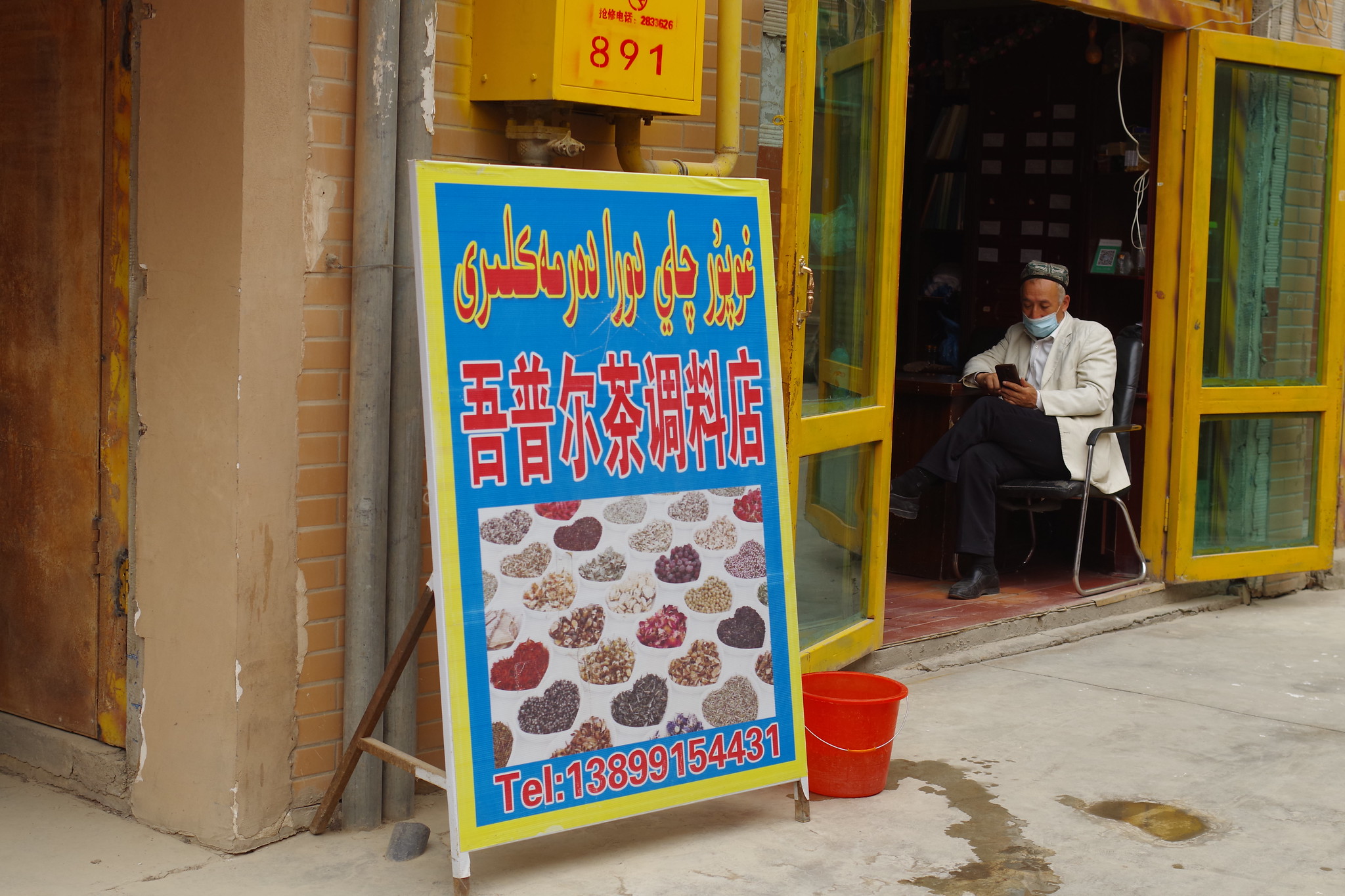 Hombre de etnia uigur, sentado en el interior de su negocio de especias y condimentos de la parte antigua de Kashgar, Xinjiang. Fotografía de Conder Kong.